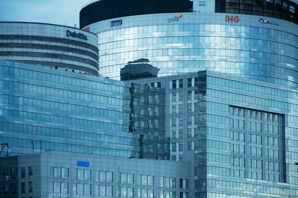 Deloitte vs PwC in un moderno edificio per uffici, con i loghi delle quattro principali società di consulenza al mondo: Deloitte, PwC, KPMG ed EY. 